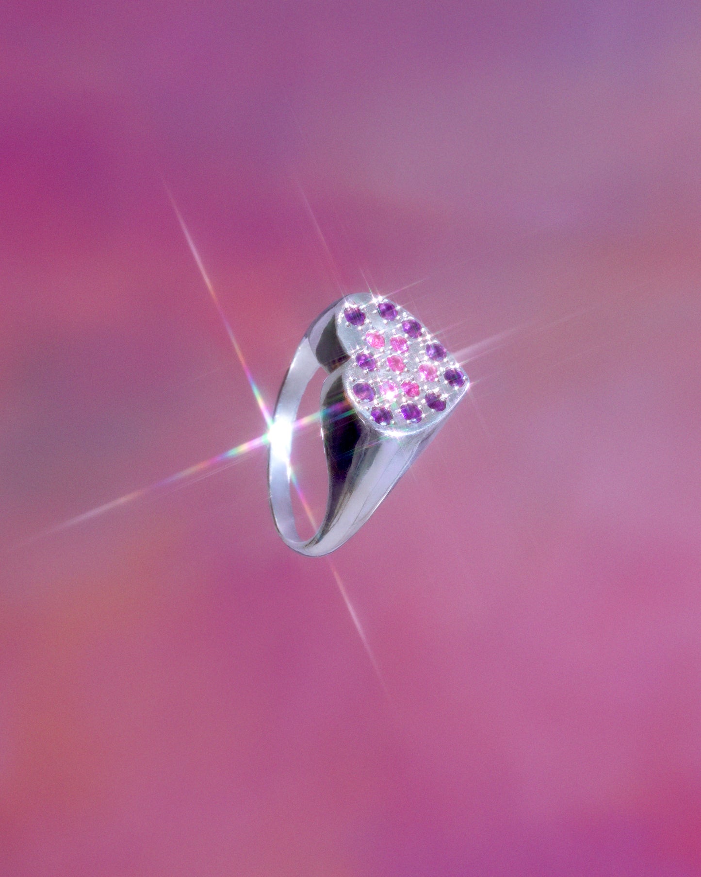 A hand sculpted heart-shaped signet ring made from responsible jewelry council certified sterling silver. The surface of the ring is set with amethysts and pink sapphirew. Handmade by Violette Stehli. Photo by Julia Grandperret Motin.