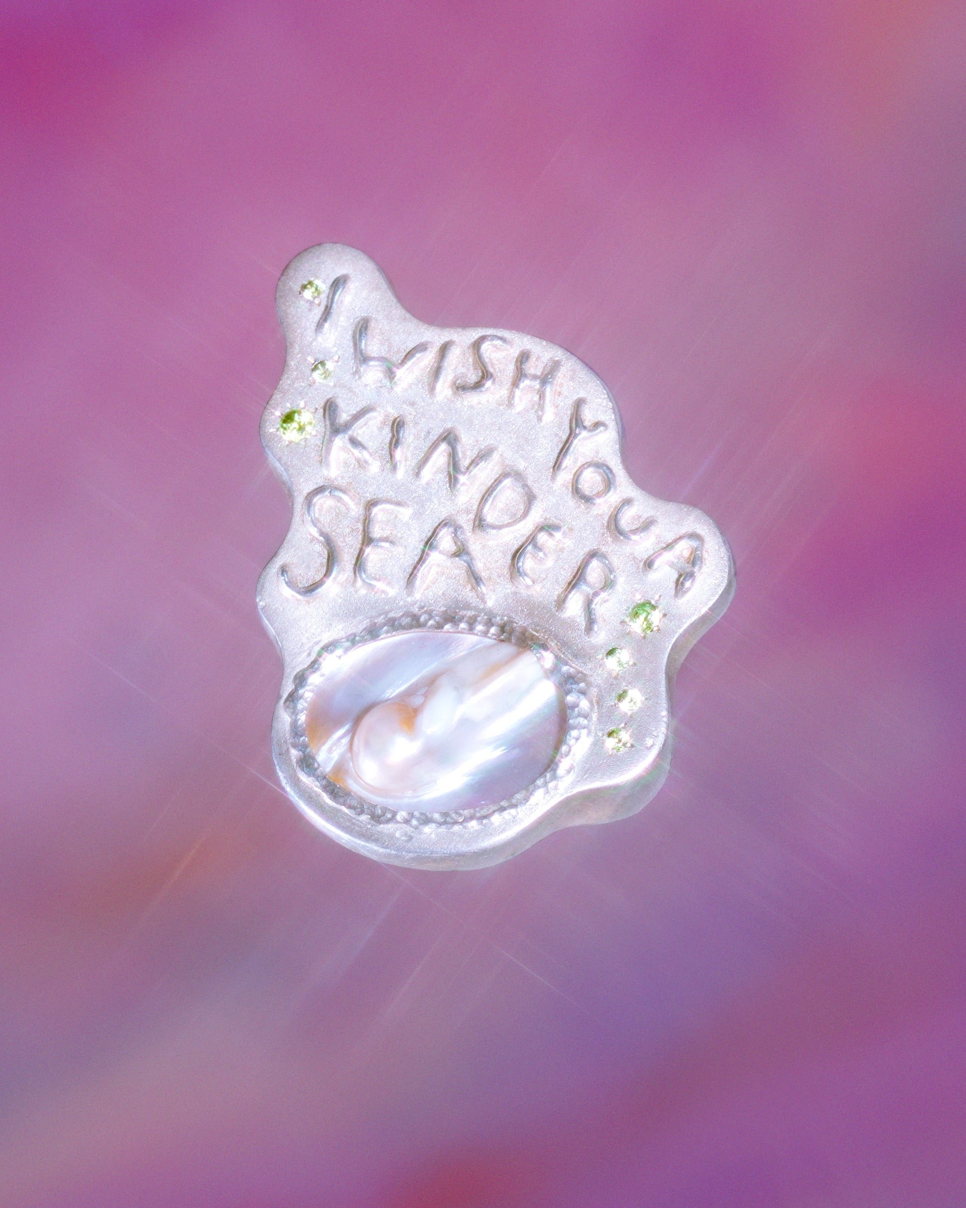 A large silver ring made from responsible jewellery council certified sterling silver, a pearl and set with peridot stones. The ring features a quote by Emily Dickinson that ready: I Wish You A Kinder Sea. The ring is hand-sculpted by Violette Stehli and photographed by Julia Grandperret Motin.