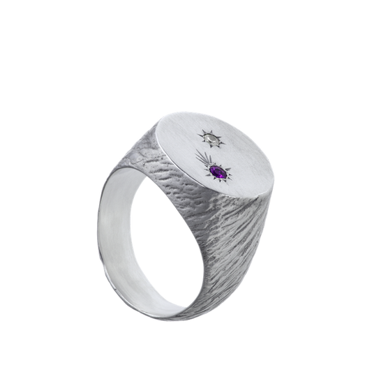 A roughly textured round signet ring made from sterling silver and set with two precious gems.