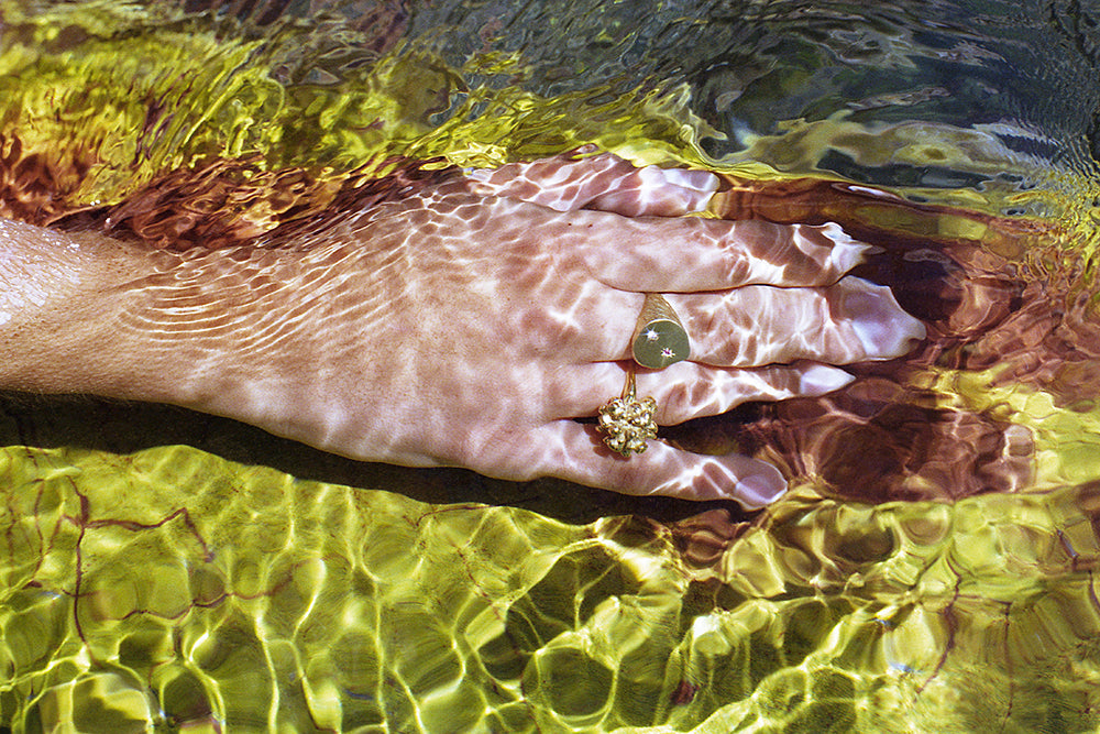 A photo of a hand under water wearing a coral ring and a signet ring by Violette Stehli. Photo By Angélique Stehli.