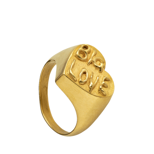 A large 18-karat gold heart-shaped signet ring with Big Love written on its surface. The font is evocative of psychedelic posters. Handmade by Violette Stehli.