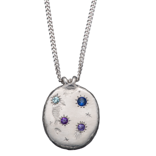 A precious but rough sterling silver medallion set with four precious stones and celestial engravings.
