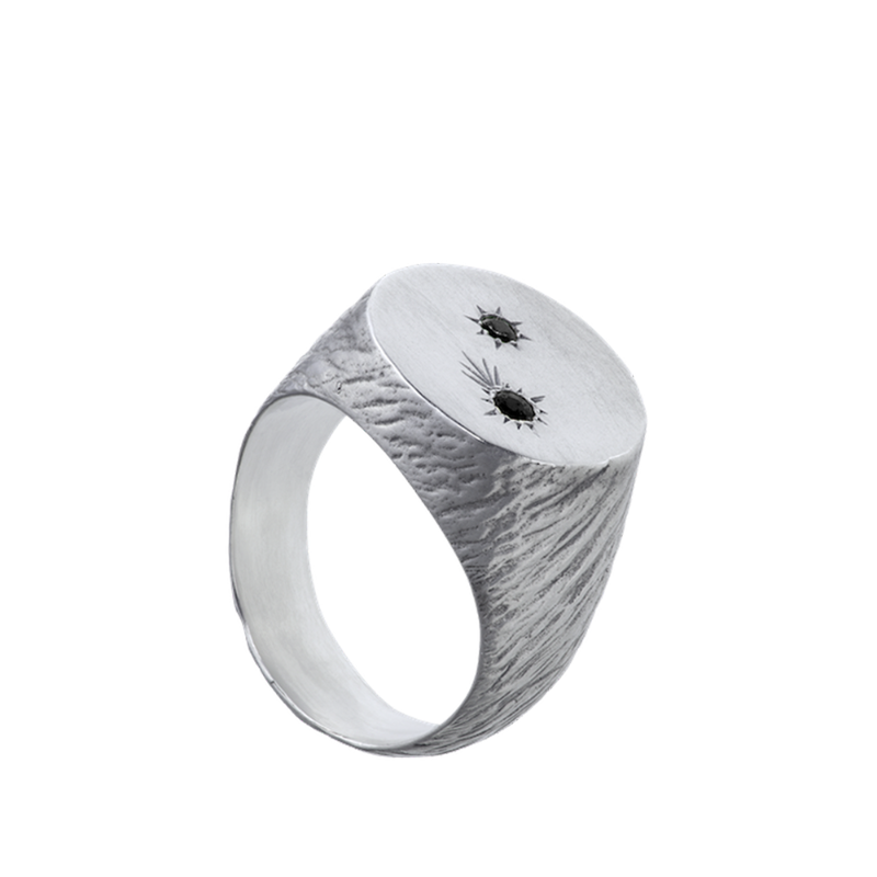 A roughly textured round signet ring made from sterling silver and set with two precious gems.
