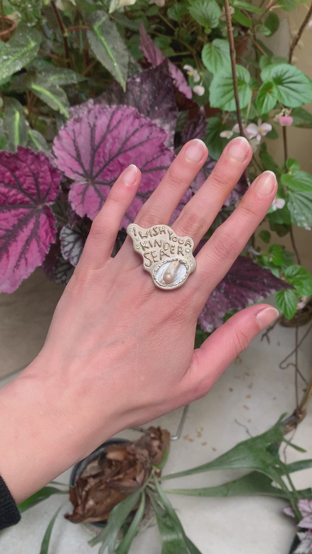 A large silver ring made from responsible jewellery council certified sterling silver, a pearl and set with peridot stones. The ring features a quote by Emily Dickinson that ready: I Wish You A Kinder Sea. The ring is hand-sculpted by Violette Stehli.
