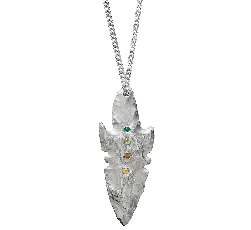 A pendant made from the cast of a neolithic era arrowhead. It is set with emerald, green and yellow sapphire and citrine on a curb-link chain. Handmade by Violette Stehli