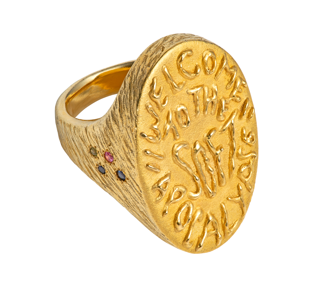A massive gold vermeil ring made by Violette Stehli. Set with sapphires and peridot and embossed with handwritten text that reads "welcome to the soft apocalypse".